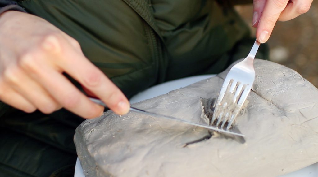 Photograph of a knife and fork being used to cut up clay